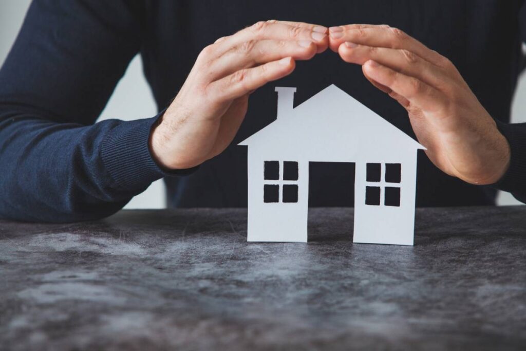 Protection d'une maison en papier par des mains.