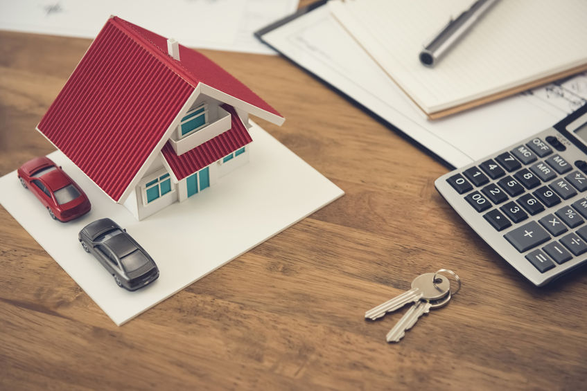 Modèle maison, clés, voitures et calculatrice sur table.